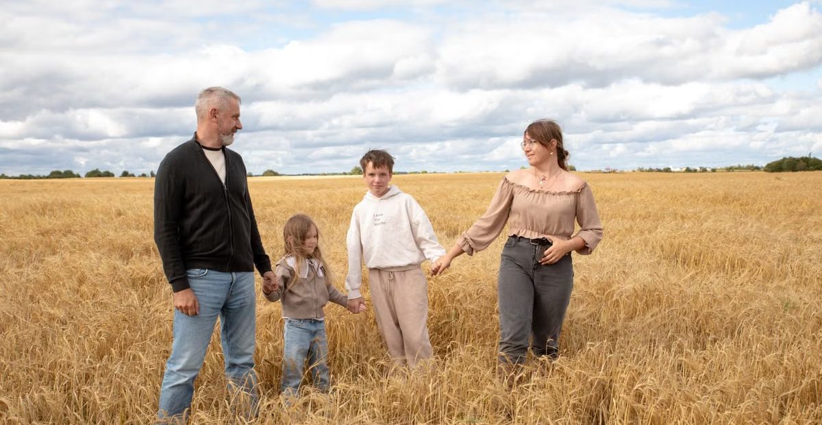 Happy family walking hand in hand through a golden wheat field on a sunny day.