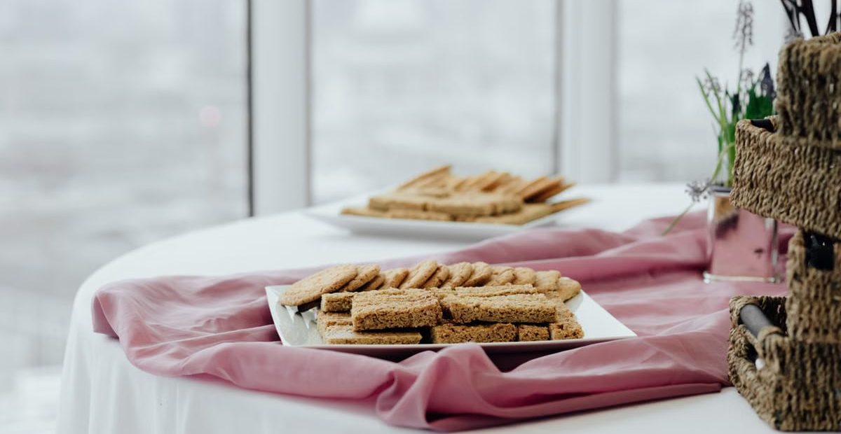 Delicious breakfast served in square shaped plates on pink fabric on blurred background of window